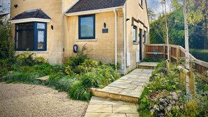 A two-story house with a stone facade, a front porch, and a garden with a gravel pathway. - Birch House (Corsham)