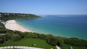 A coastal view with a sandy beach, a clear blue sea, and a grassy area with a pathway leading to the beach. - Glas Mor (St Ives)