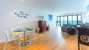 A modern living room with a dining area, large windows, and a view of the sea. - Glas Mor (St Ives)