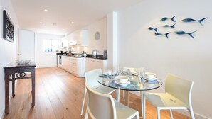 A modern kitchen with white cabinets and a dining area with a glass table and white chairs. - Glas Mor (St Ives)