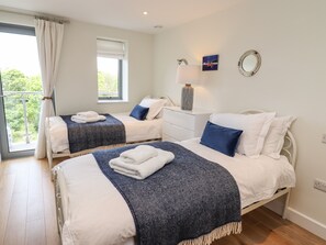 A hotel room with two beds, a window with curtains, a nightstand with a lamp, and a small painting on the wall. - Bamaluz (St Ives)