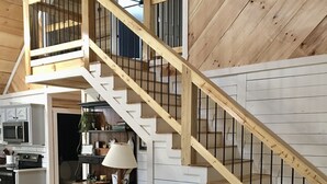 Un salon chaleureux avec un escalier en bois, un canapé, une table basse en verre et un fauteuil.