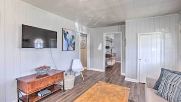 Un salon avec une table basse en bois, un canapé blanc, un téléviseur fixé au mur et un meuble en bois.