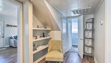 A hallway with a beige armchair, white shelves with decorative items, and a metal rack.