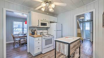 A kitchen with white cabinets, a microwave, a refrigerator, a stove, and a ceiling fan.
