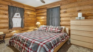 Une chambre située dans un chalet en rondins, avec un lit, un ventilateur de plafond, une table de chevet et une commode.