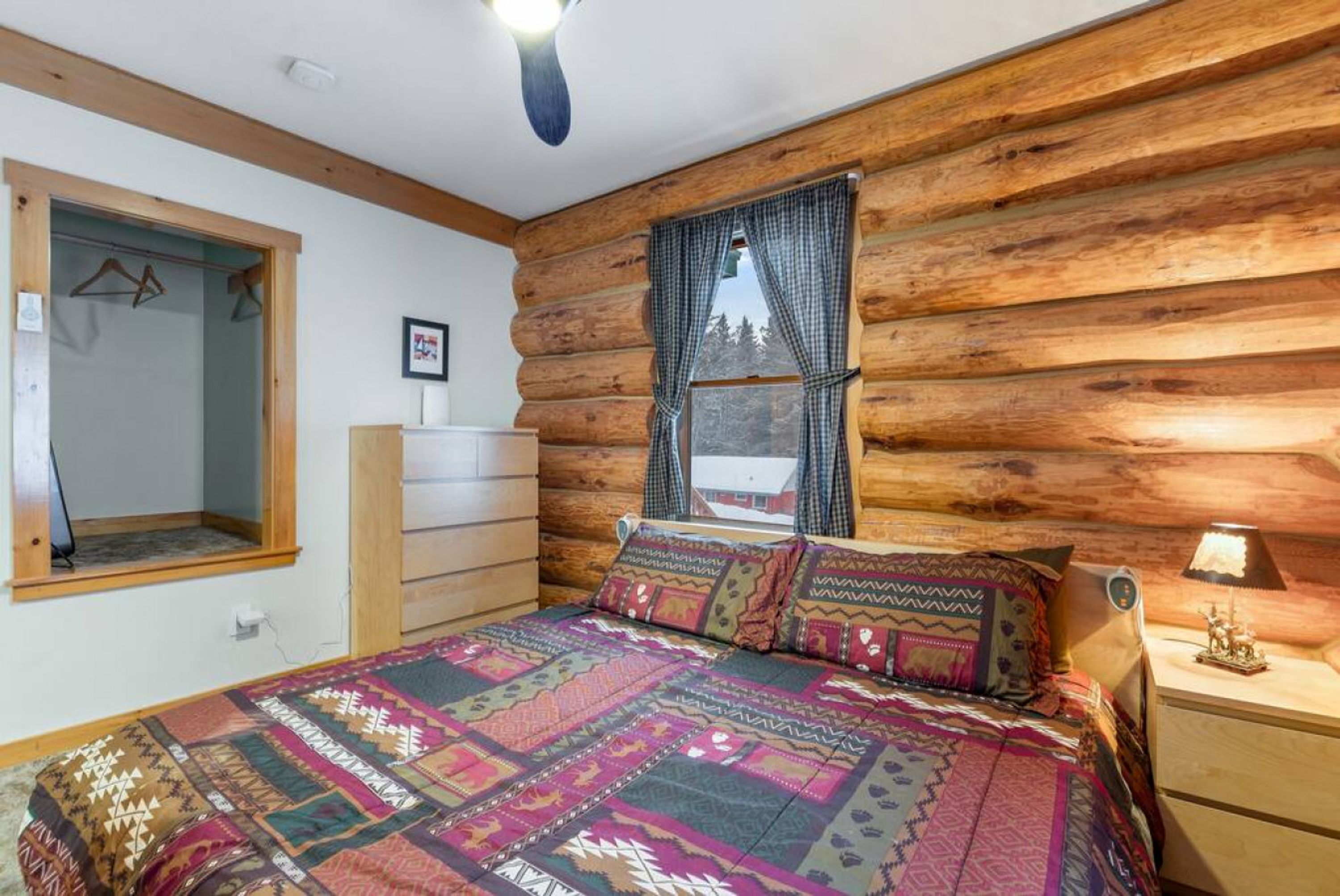 Un dormitorio rústico de madera con una cama grande, un aparador, una ventana con cortinas y una lámpara colgante.