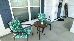 A covered porch with two chairs and a table, a door with a wreath, and a sign that reads "HOME Sweet HOME". - Masters Rental (Aiken)