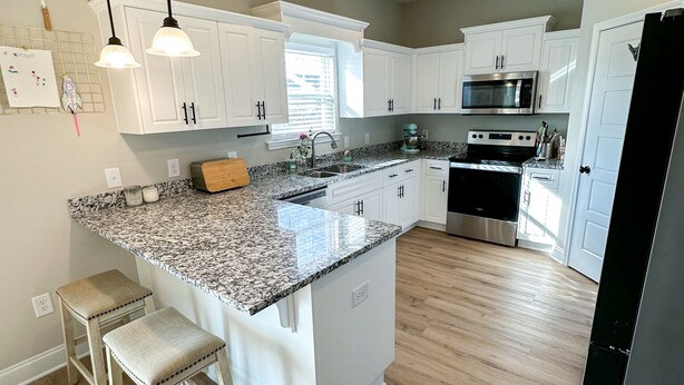 A modern kitchen with white cabinets, granite countertops, stainless steel appliances, and a central island with bar stools. - Masters Rental (Aiken)