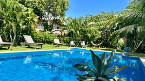 Piscina com água azul cristalina, rodeada por espreguiçadeiras e plantas tropicais.