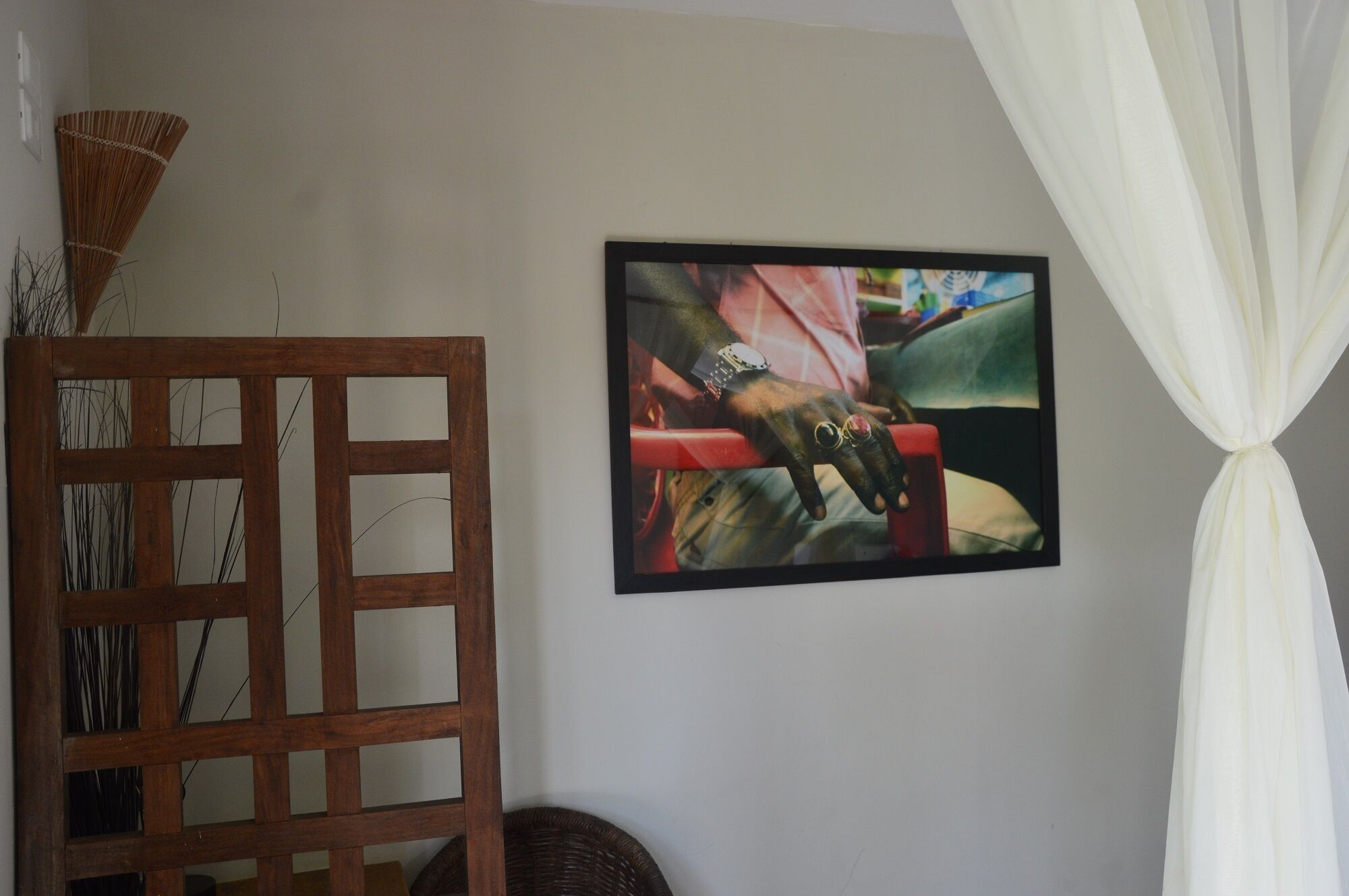 Um quarto com uma cadeira de madeira, um quadro na parede e uma cortina branca.