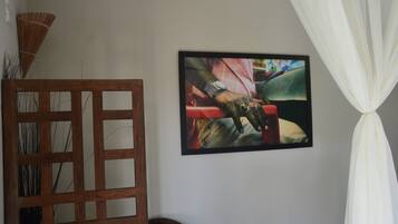 Um quarto com uma cadeira de madeira, um quadro na parede e uma cortina branca.