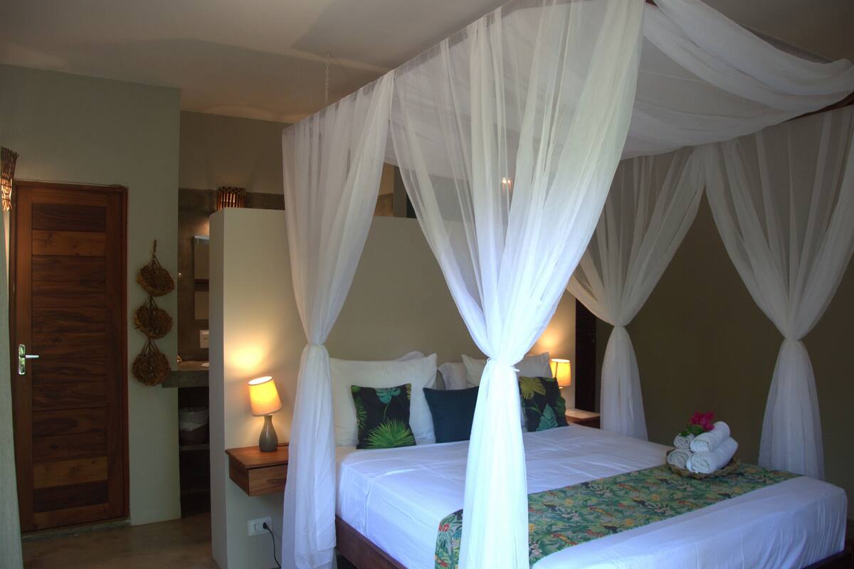 A four-poster bed with white drapes, a bedside lamp, and a floral bedspread.