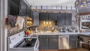 A modern kitchen with dark cabinets, a white stove, and a stone backsplash. - Beautiful Victorian in Downtown Cheboygan (Cheboygan)
