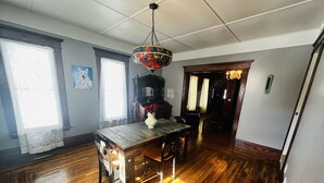 A dining area with a wooden table and chairs, a decorative hanging light fixture, and a vase with flowers. - Beautiful Victorian in Downtown Cheboygan (Cheboygan)