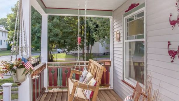 A wooden porch with two rocking chairs and a small table, decorated with American flags and a hanging plant. - Beautiful Victorian in Downtown Cheboygan (Cheboygan)