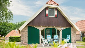 A building with a pitched roof, brick walls, and green doors. There is a table with chairs in front. - Gorgeous home in IJhorst with WiFi (IJhorst)