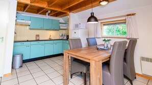 A compact kitchen with teal cabinets, a wooden dining table, and a window with curtains. - Gorgeous home in IJhorst with WiFi (IJhorst)
