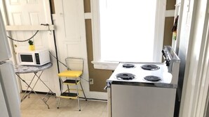 Una cocina compacta con estufa, microondas y una mesita con una silla.