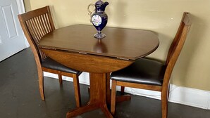 Una mesa de madera para comer con dos sillas, una jarra decorativa y una pared beige al fondo.
