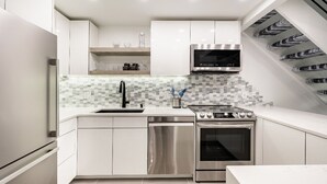 A modern kitchen with white cabinetry, a stainless steel range hood, a microwave, and a dishwasher. - Modern & Unique Pearl street condo (Boulder)