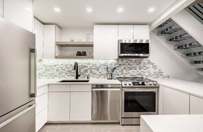 A modern kitchen with white cabinetry, a stainless steel range hood, a microwave, and a dishwasher. - Modern & Unique Pearl street condo (Boulder)