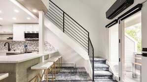 A modern kitchen with a concrete island, bar stools, and a black staircase. - Modern & Unique Pearl street condo (Boulder)