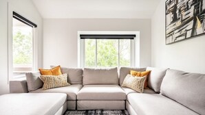 A modern living room with a sectional sofa, a large window with blinds, and a piece of abstract art on the wall. - Modern & Unique Pearl street condo (Boulder)