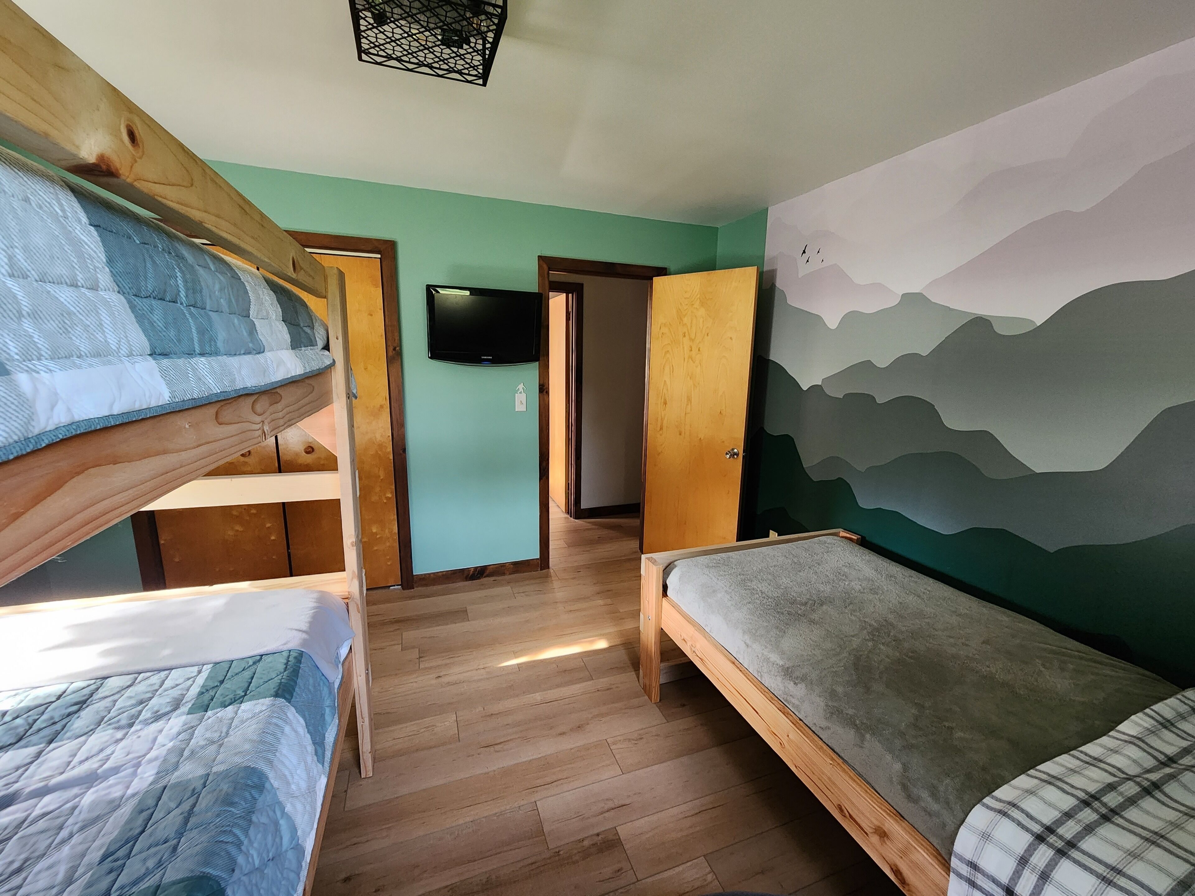 A room with bunk beds, a flat-screen TV, and a mountain mural on the wall.