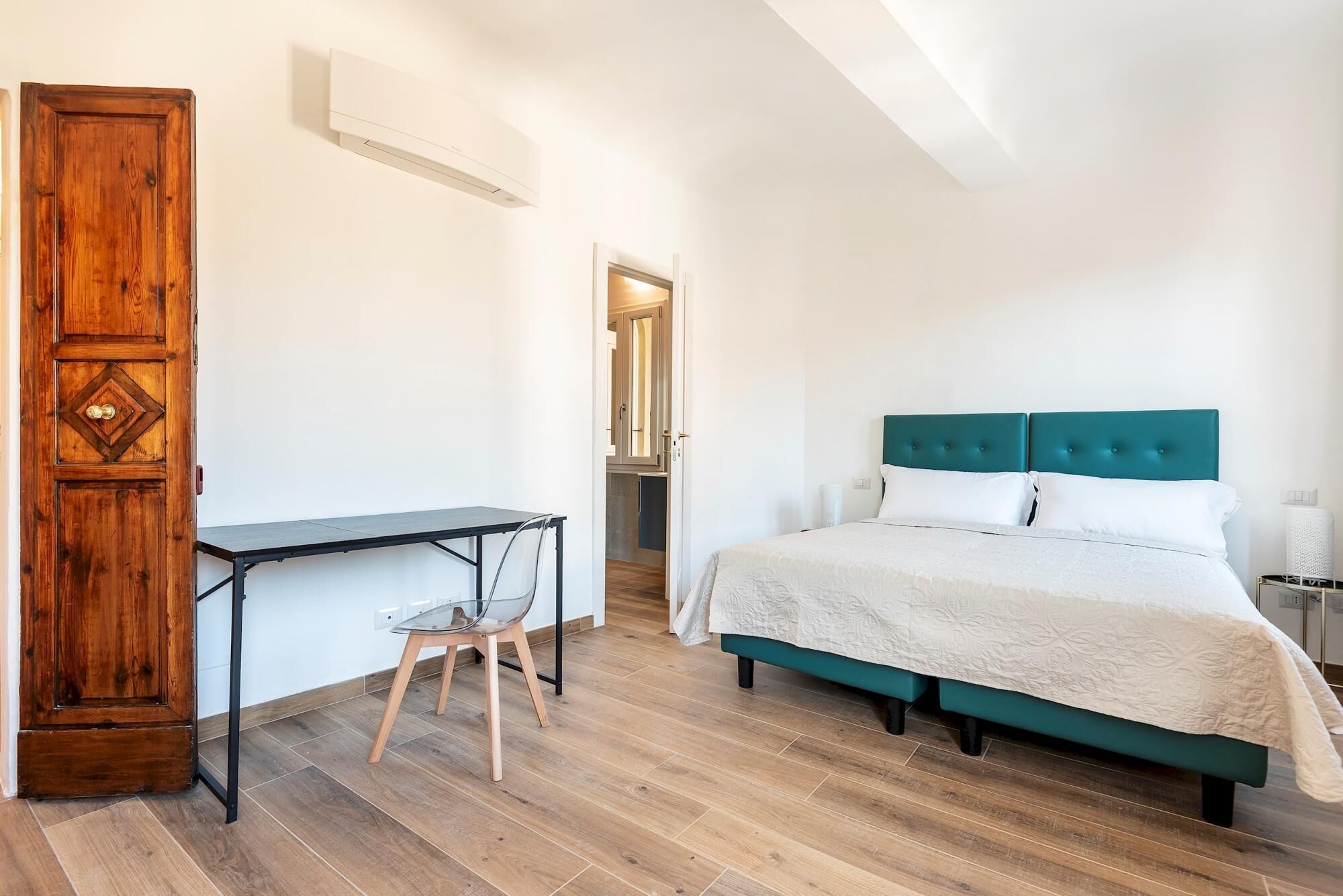 A bedroom with a bed, a desk, and a wardrobe.