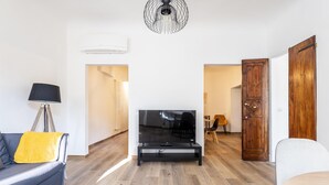 A living room with a flat-screen TV on a stand, a sofa with a yellow pillow, a lamp, and a wooden floor. - Alloro Apartment in Firenze (Florence)
