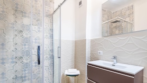A bathroom with patterned tiles, a glass shower enclosure, a sink with a mirror, and a small stool. - Alloro Apartment in Firenze (Florence)