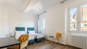 A modern bedroom with two beds, a dining table, and a chair. - Alloro Apartment in Firenze (Florence)