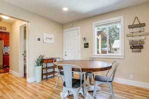A dining area with a round table and four chairs, a kitchen with red cabinets, a white door, and motivational wall art.