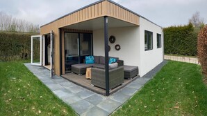 Een modern huis met een overdekte patio, een zithoek en een bord met de tekst 'SE SANS SAISON'.
