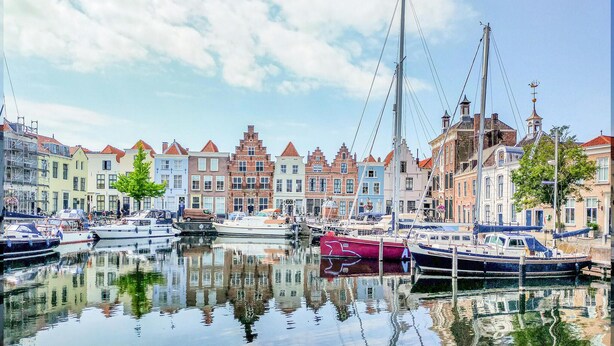 Een jachthaven met aangemeerde boten, omgeven door historische gebouwen met verschillende bouwstijlen.