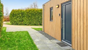 Een modern gebouw met een houten gevel, een verhard pad naar de ingang en een verzorgde haag op de achtergrond.