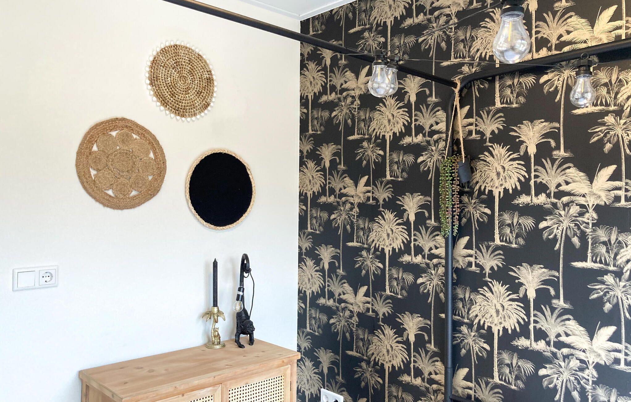 Une pièce dont le papier peint représente des palmiers en noir et blanc, avec une armoire en bois et trois appliques murales.