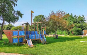 Children can play and climb in this multi-level play area surrounded by a lush green field and trees.