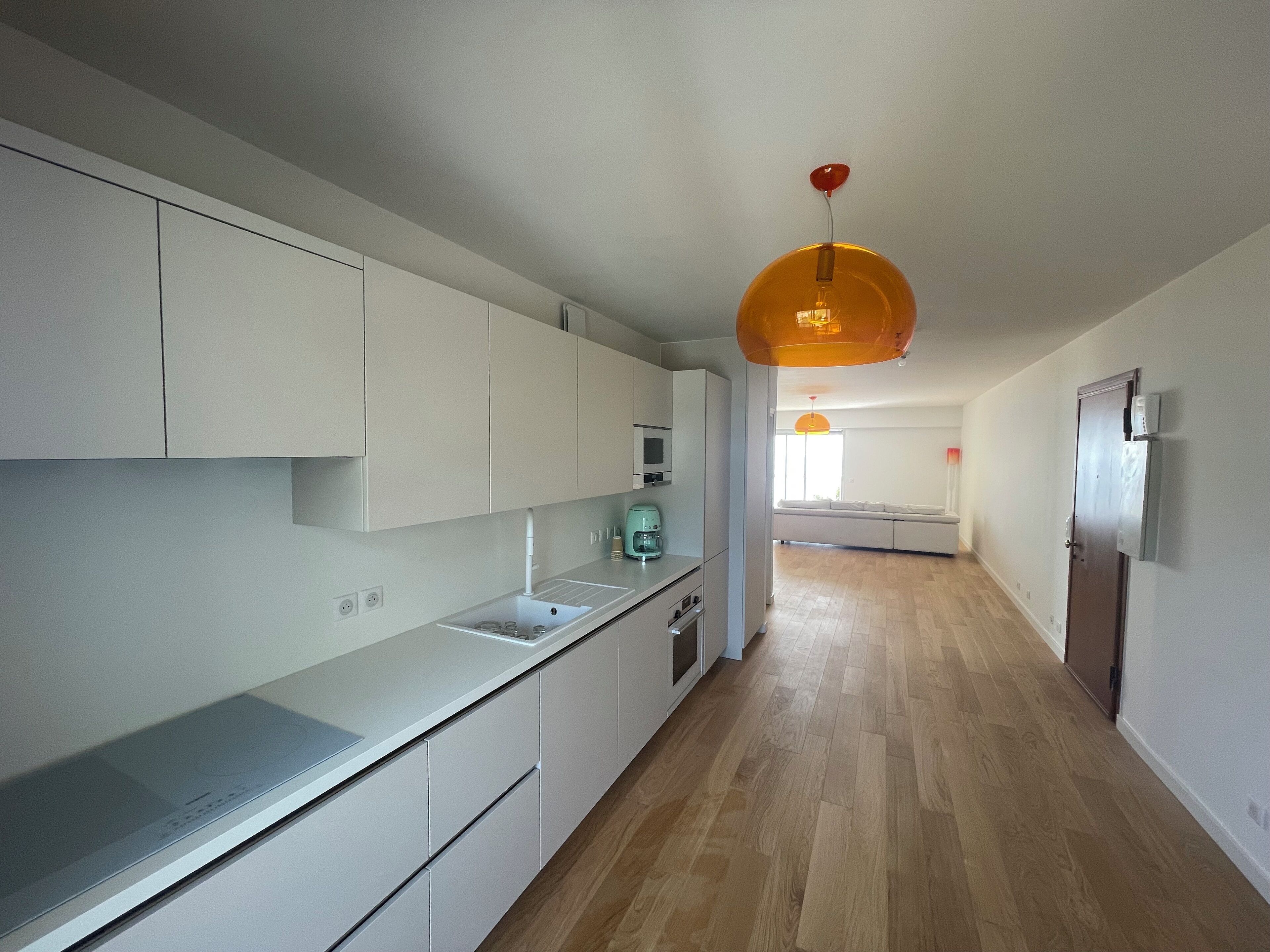 Een moderne keuken met witte kastjes, een houten vloer en een hanglamp.