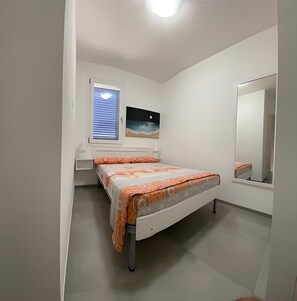 Cozy retreat with a single bed, bedside table, and nightstand, featuring a painting above the bed and a full-length mirror.
