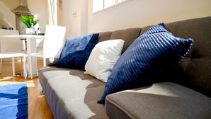 Ein Wohnzimmer mit einer Couch, zwei Kissen, einem Couchtisch und einem Essbereich mit Stuhl und Tisch.