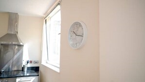 Eine Küche mit einer Edelstahl-Dunstabzugshaube, einem Fenster mit Jalousien und einer Wanduhr.