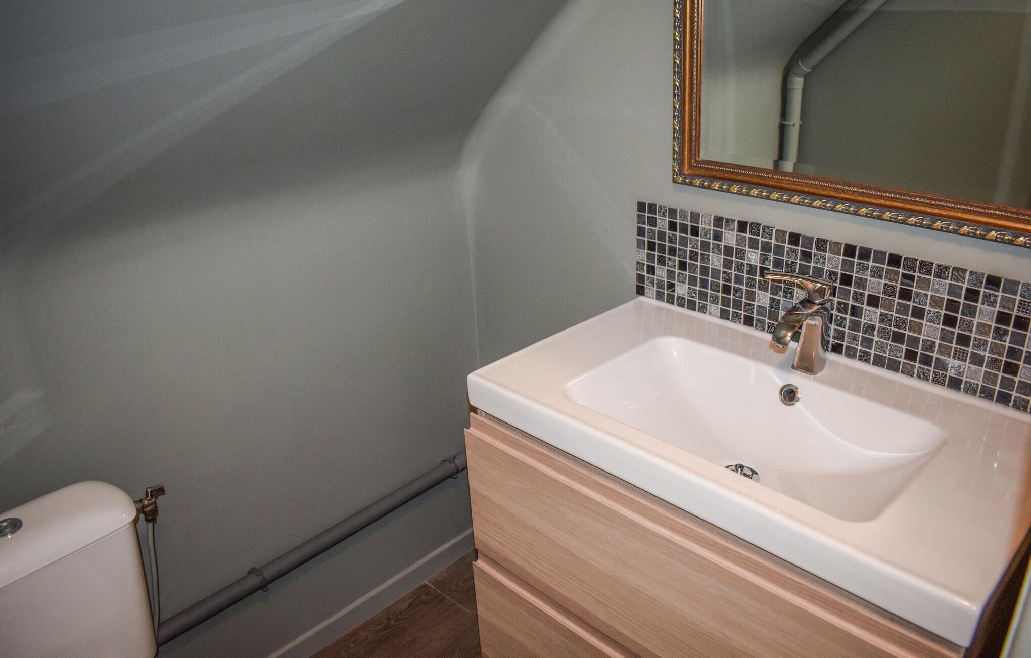 Un baño con un lavabo blanco, un armario de madera y un revoque de azulejos.