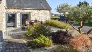 Un edificio de piedra con un patio, mobiliario exterior y un jardín con diversas plantas y un árbol.