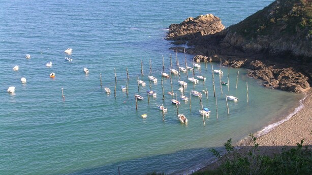 Zona costera con barcos anclados cerca de la orilla, rodeada de terreno rocoso y vegetación.