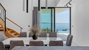 Un comedor moderno con vista al mar, una escalera y un puerta de cristal que da al exterior.