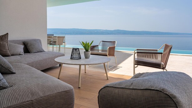 Un área de estar moderna al aire libre con piscina, vistas al mar y un balcón con sofá y sillones.