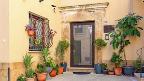 A building entrance with a door, potted plants, and a window with a metal railing. - L'Antro di Dedalo (Sciacca)