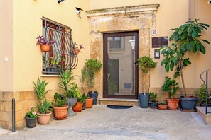 A building entrance with a door, potted plants, and a window with a metal railing. - L'Antro di Dedalo (Sciacca)